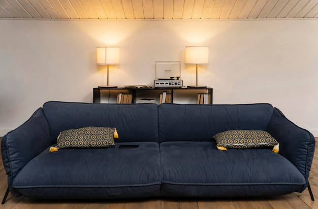Темно-синий диван с узорчатыми подушками в уютной обстановке гостиной с двумя лампами на консольном столике на заднем плане.